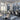 Elegant restaurant interior featuring marble-look flooring and wall panels, modern round tables, upholstered chairs, floral centerpieces, and artistic bubble chandeliers with large windows letting in natural light.